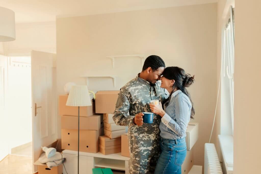 Happy wife and her african american army veteran husband in camouflage clothing with cardboard boxes