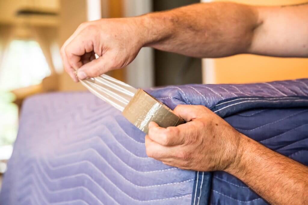 A mover tapes a padded blanket around a piece of furniture