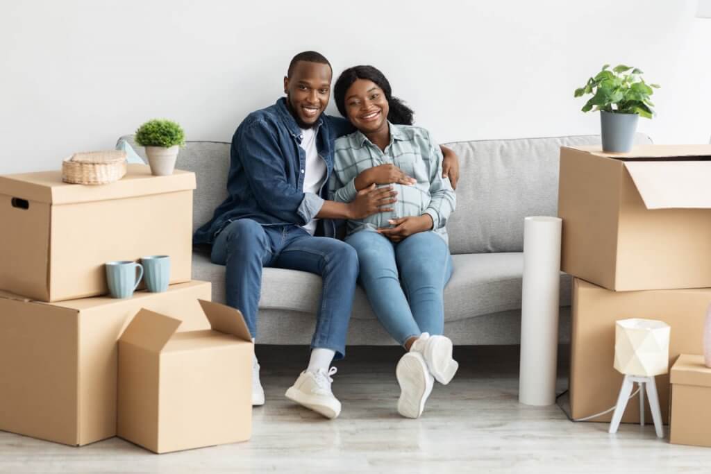 Happy Pregnant Couple Relaxing On Couch After Moving To New Apartment