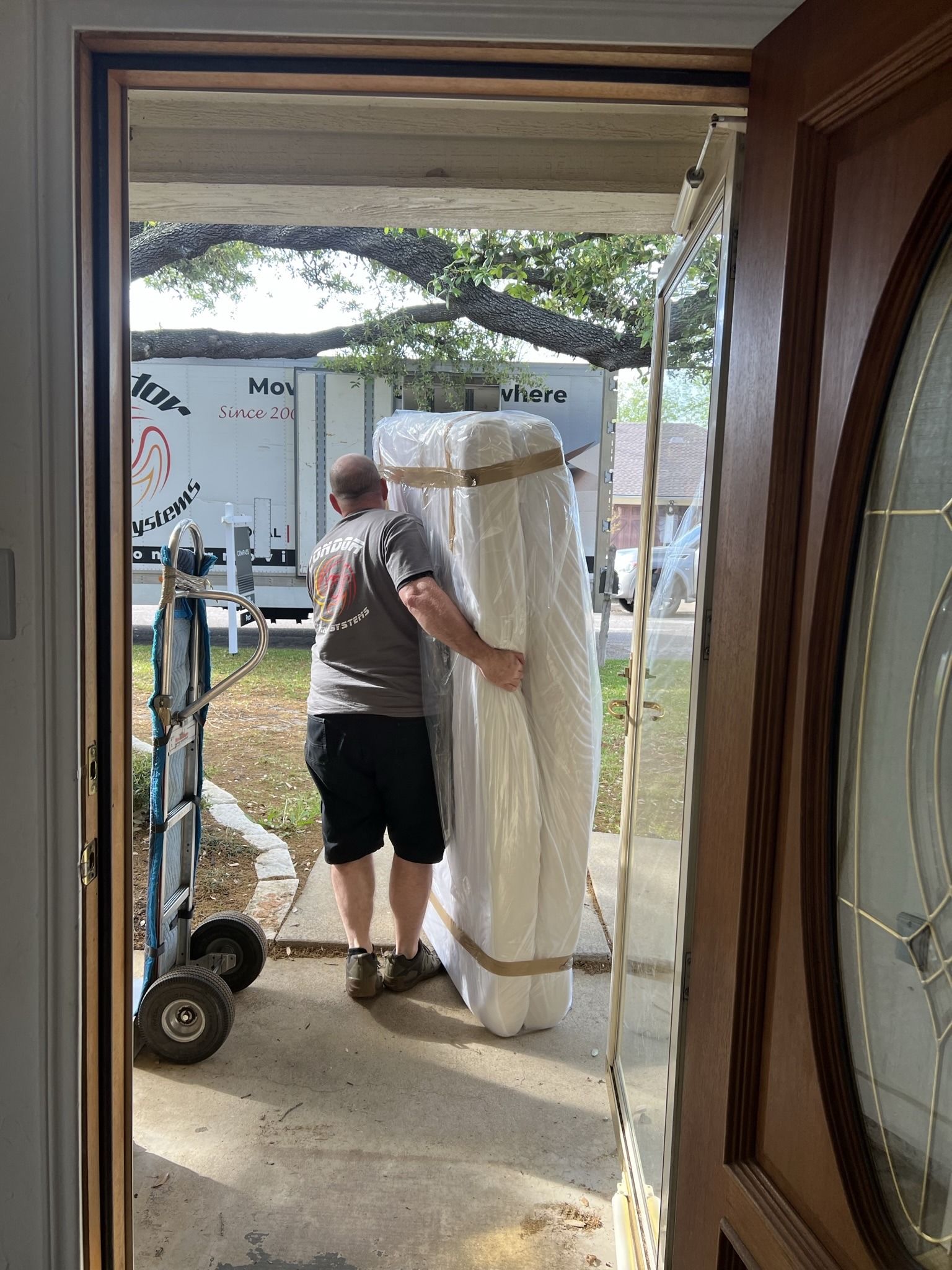 Condor mover carrying a plastic-wrapped mattress out the front door to the moving truck